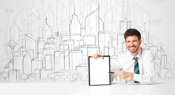 Üzletember ül a fehér asztalnál kézzel rajzolt épületekkel — Stock Fotó