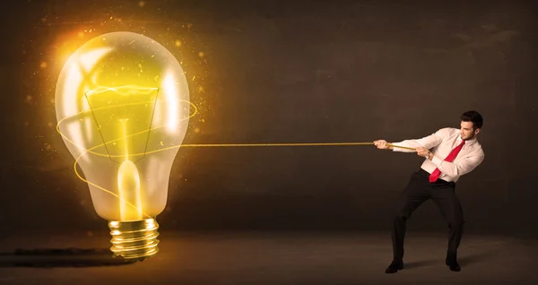 Business man pulling a big bright glowing light bulb — Stock Photo, Image