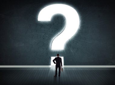 Parlak bir soru işaretiyle duvara bakan bir iş adamı 
