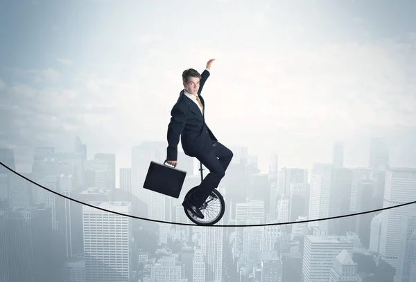 Brave guy riding a monocycle on a rope above cityscape — Stock Photo, Image