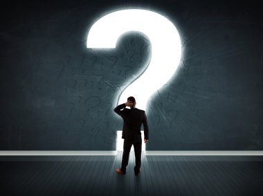 Parlak bir soru işaretiyle duvara bakan bir iş adamı