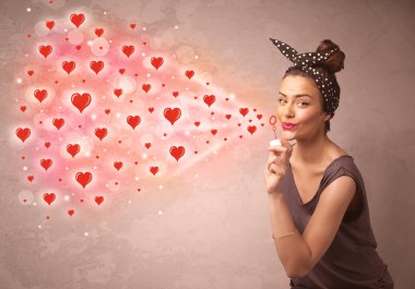 Güzel genç kız kırmızı kalp sembolleri üflüyor.