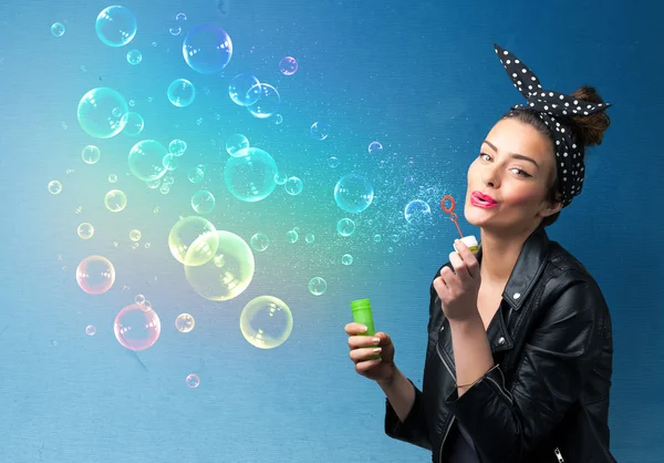 Гарненька леді дме барвисті бульбашки на синьому фоні — стокове фото