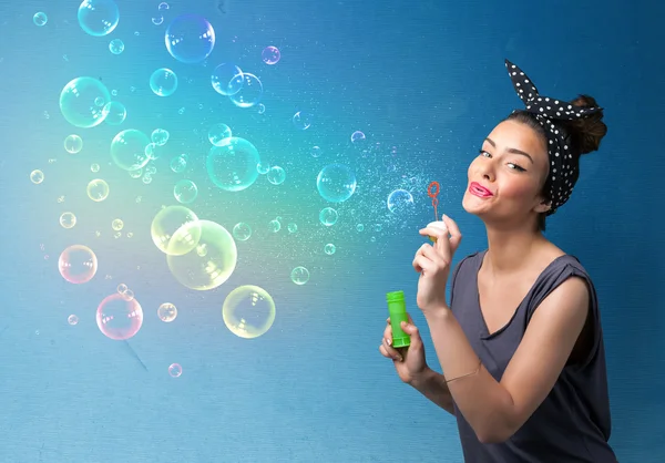 Bonita dama soplando burbujas de colores sobre fondo azul — Foto de Stock