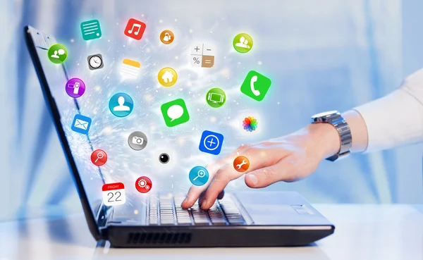 Mão pressionando laptop moderno com ícones e símbolos de aplicativos móveis — Fotografia de Stock