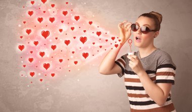 Güzel genç kız kırmızı kalp sembolleri üflüyor.