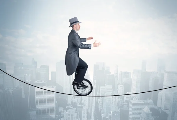 Brave guy riding a monocycle on a rope above cityscape — Stock Photo, Image