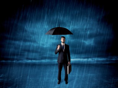 İş adamı elinde şemsiyeyle yağmurda duruyor.