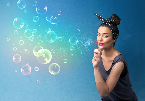 Pretty lady blowing colorful bubbles on blue background — Stock Photo, Image