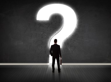 Parlak bir soru işaretiyle duvara bakan bir iş adamı 