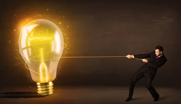 Business man pulling a big bright glowing light bulb — Stock Photo, Image