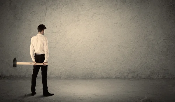 Business man standing in front of a grungy wall with a hammer — Stock Photo, Image