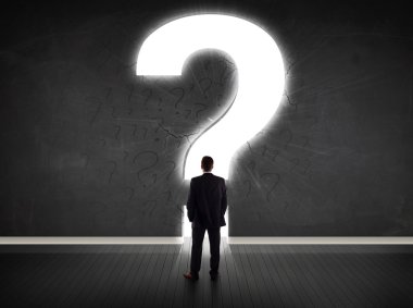 Parlak bir soru işaretiyle duvara bakan bir iş adamı 