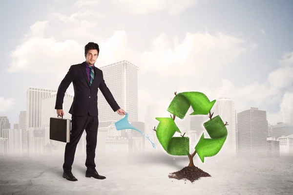 Homem de negócios molhando árvore sinal de reciclagem verde no fundo da cidade — Fotografia de Stock
