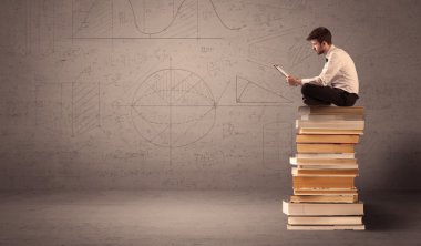 Tabletli bir iş adamı kitapların üzerinde oturuyor.