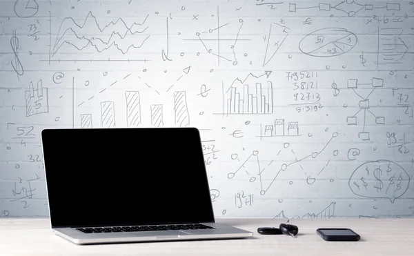 Ноутбук на столе с бизнес-диаграммами на стене — стоковое фото
