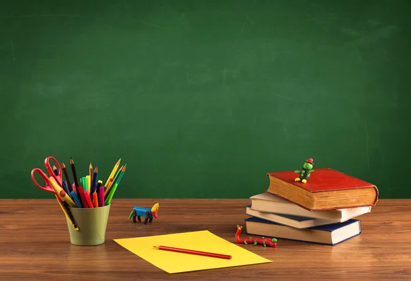 Schoolspullen op bureau met leeg schoolbord — Stockfoto