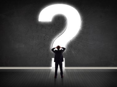 Parlak bir soru işaretiyle duvara bakan bir iş adamı 