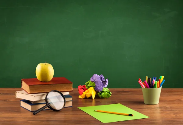 Itens escolares na mesa com quadro-negro vazio — Fotografia de Stock