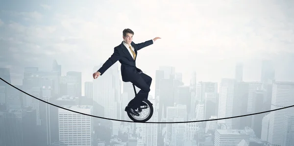 Valiente tipo montando un monociclo en una cuerda por encima del paisaje urbano — Foto de Stock