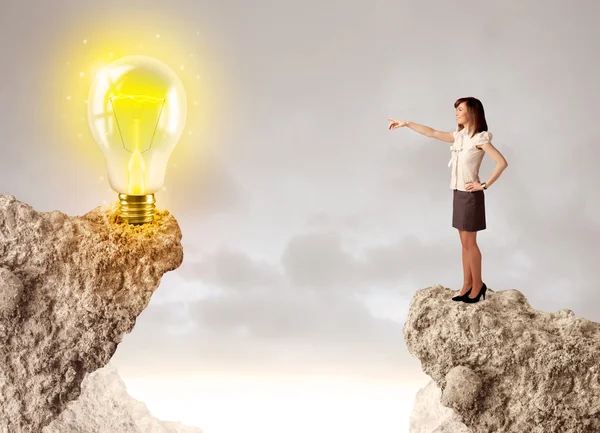 Businesswoman on rock mountain with idea bulb — Stock Photo, Image