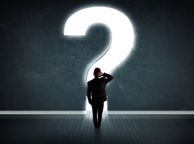 Parlak bir soru işaretiyle duvara bakan bir iş adamı 