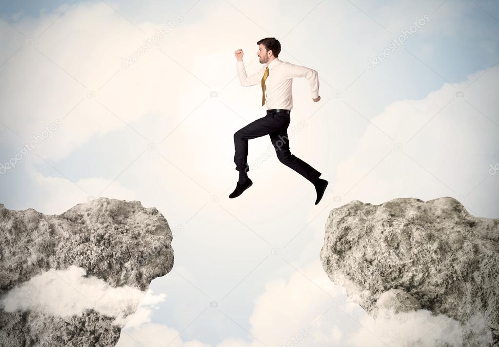 Happy business man jumping over a cliff 