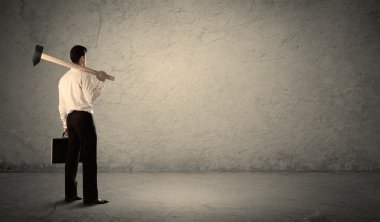 Pis bir duvarın önünde elinde çekiçle duran bir iş adamı.