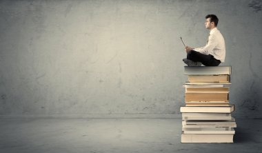 Adam kitaplar üzerinde oturan dizüstü bilgisayar ile
