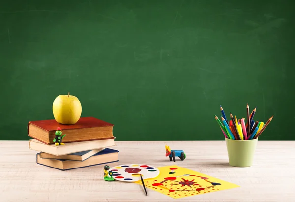 Itens escolares na mesa com quadro-negro vazio — Fotografia de Stock