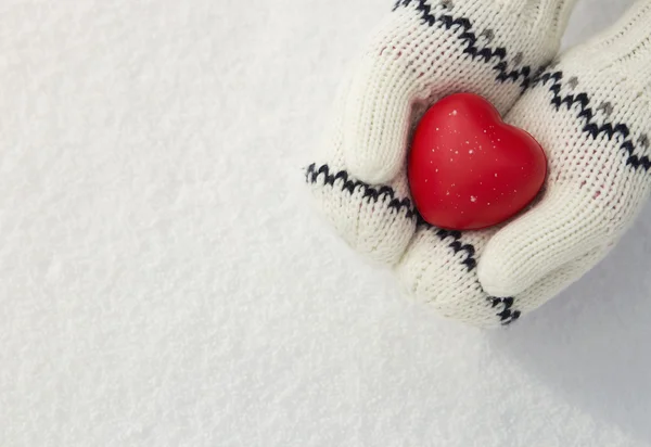 Mãos de menina segurando coração vermelho na neve — Fotografia de Stock