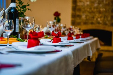 Ekmek sepeti, şarap kadehleri ve kırmızı hediye süslemeleri ile şık bir sofra. Kutlama veya aile yemeği için sıcak bir ortam yaratıyor..