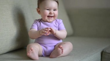 Bebek kız gülümsüyor ve evde kanepede oturan gülüyor
