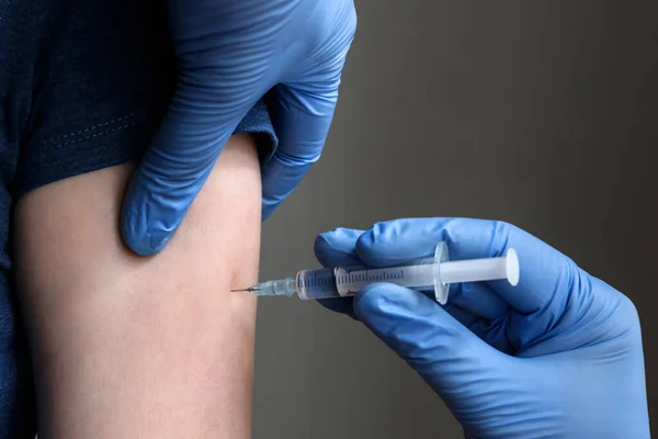 Vaccine injection close-up, doctor in gloves holds syringe and makes jab to patient arm. Prevention of COVID-19 coronavirus or influenza. Concept of corona virus and flu shot, therapy, clinical trial.