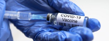 Doktorun elinde COVID-19 koronavirüs aşısı, Corona virüsü tedavisi için panoramik bir şırınga ve aşı şişesi. Salgın sırasında tedavi, iğne, aşı ve klinik deney kavramı.