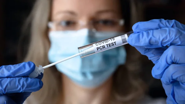 Coronavirus swab collection kit in doctor hands, woman in medical face mask holding tube of COVID-19 PCR test in laboratory. Concept of corona virus diagnostics, testing and treatment during pandemic