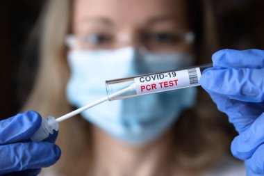 COVID-19 PCR testi doktorun ellerinde, yüz maskeli hemşire laboratuarda koronavirüs temizleme kiti tutuyor. Salgın sırasında korona virüsü teşhisi, tıbbi test ve tedavi kavramı.