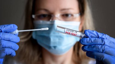 Coronavirus örnek toplama kiti doktorun ellerinde, tıbbi maskeli kadın COVID-19 PCR tüpünü laboratuvarda tutuyor. COVID salgını sırasında korona virüsü teşhisi, test ve tedavi kavramı.