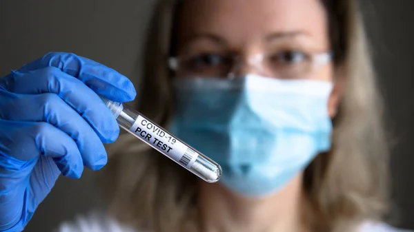 COVID-19 PCR test tube in doctor hand, woman in medical mask holds coronavirus swab collection kit in lab. Concept of corona virus diagnostics, testing and treatment during coronavirus pandemic.