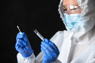 Coronavirus örnek toplama kiti doktorun ellerinde, tıbbi kişisel koruyucu ekipman hemşiresi (PPE) koyu arkaplanda COVID-19 PCR testi yapıyor. Corona virüsü testi ve teşhisi.