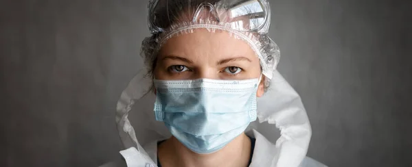 Woman wearing protective glasses and medical face mask due to COVID-19 coronavirus pandemic, panoramic banner with portrait of female doctor or nurse in PPE suit. Concept of corona virus and uniform.