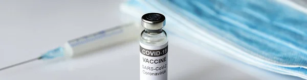 COVID-19 vaccine injection, panoramic banner with syringe, medical masks and bottle of vaccine for coronavirus. Concept of health, corona virus treatment, vaccination and distribution during pandemic.