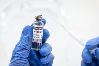 Doktorun eldivenli eline, şırıngasına ve aşı şişesine beyaz arka planda enjeksiyon için COVID-19 koronavirüs aşısı. Salgın sırasında aşı, tıbbi iğne ve korona virüsü tedavisi kavramı.