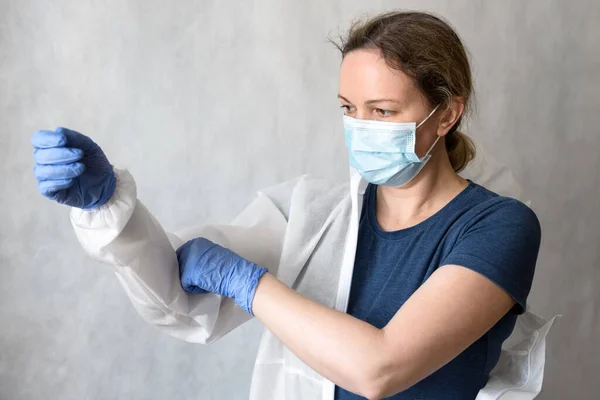 Doctor puts on personal protective equipment (PPE) due to COVID-19, female nurse with medical coverall for coronavirus, woman physician holds uniform during COVID pandemic. Corona virus concept.