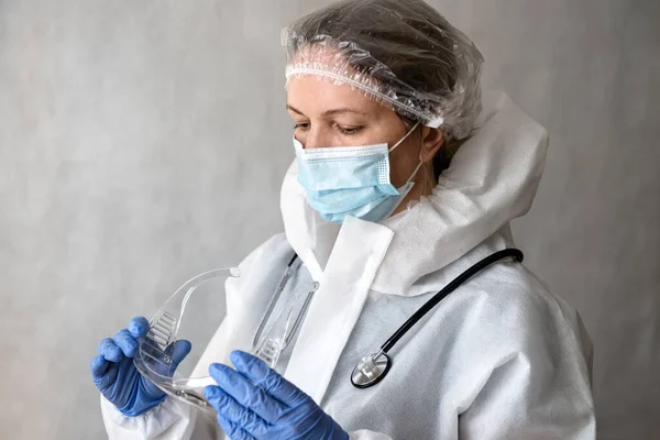 Doctor in personal protective equipment (PPE) from COVID-19, portrait of tired woman physician in medical coverall due to coronavirus, female doctor with suit, mask and glasses. Corona virus concept.