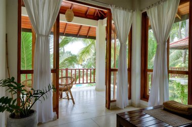 Tangalle, Sri Lanka - Nov 2, 2017: Hotel or residential house in tropical garden, room with terrace, windows and sea beach view. Home interior in Indian minimalist style. Ocean front resort in summer