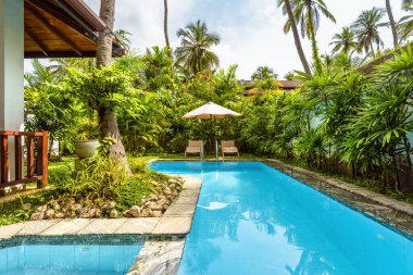 Pool with umbrella and beach beds at tropical hotel or vacation home. Beautiful swimming pool in courtyard of residential house. Landscape design of backyard. Nice landscaping garden in summer resort.