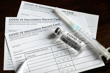 COVID-19 Vaccination Record Card on desk, coronavirus immunization certificate and vaccine injection. Syringe and vaccine bottle for corona virus are on medical form required for travel and tourism.