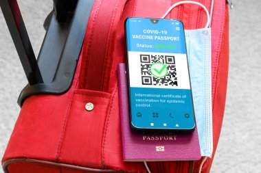 Health passport of COVID-19 vaccination in mobile phone for travel, smartphone with passport app on suitcase. Digital certificate as proof of coronavirus immunization. COVID vaccine pass and tourism.