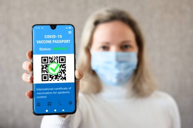 COVID-19 vaccination passport in mobile phone for travel, woman wearing mask holds smartphone with health certificate app, digital coronavirus pass. Concept of corona virus and immunity passport.